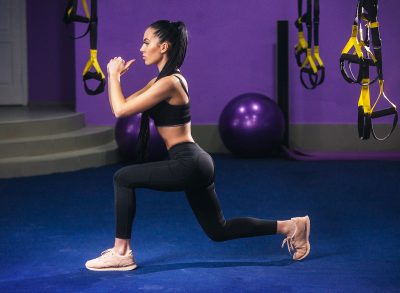 fit woman demonstrating walking lunges at gym to transform your backside