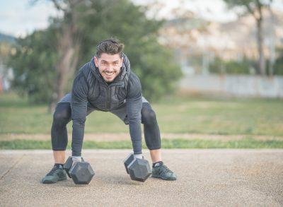 fit man performing dumbbell squats outdoors, demonstrating seven-day workout to shrink belly fat