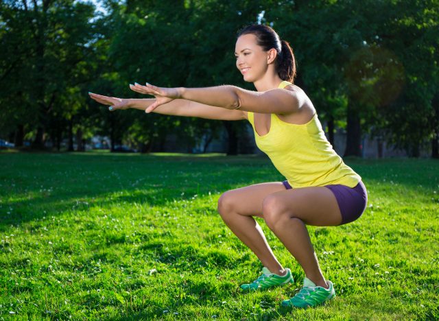 Fitness woman doing squats outdoors in the sun