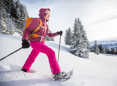 fitness woman snowshoeing through snowy mountains, demonstrating winter weight loss activities