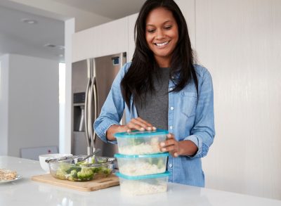 happy woman meal prepping rice and broccoli in containers, concept of habits to start losing weight this week