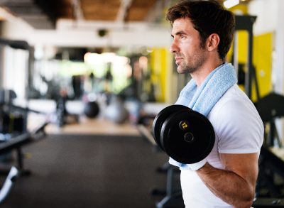 fit man doing bicep curls at the gym, close-up, concept of mistakes men make at the gym that hurt progress