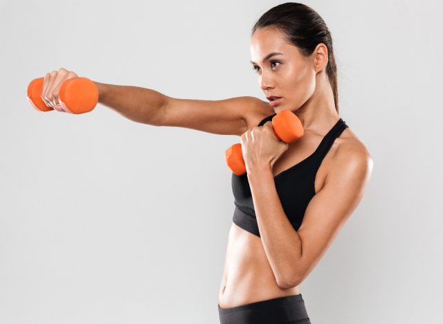 fit woman holding out orange dumbbells, concept of dumbbell exercises to lose weight in 30 days