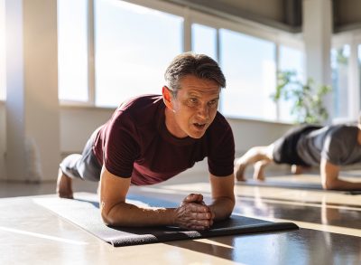 mature man doing planks during group fitness class, concept of exercise habits that destroy your back after 50