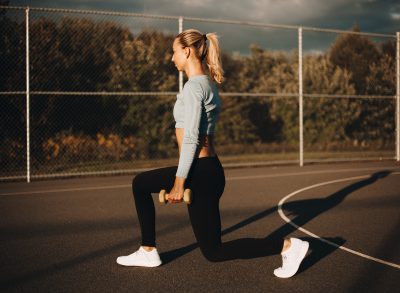 fitness woman doing 10-minute legs workout dumbbell lunges outdoors on court