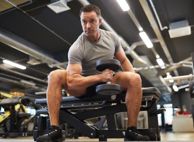 middle-aged man at the gym with defined muscles doing dumbbell arm workouts