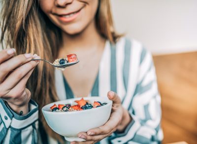 close-up woman holding bowl of oats and fruit, concept of breakfast habits to curb cravings and lose weight