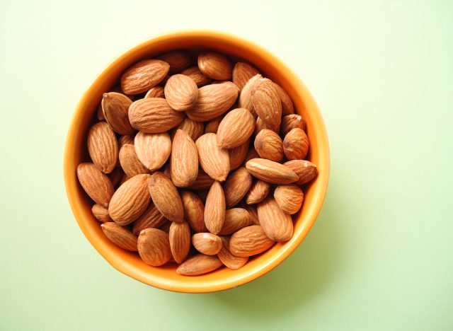 Almonds in bowl on green background
