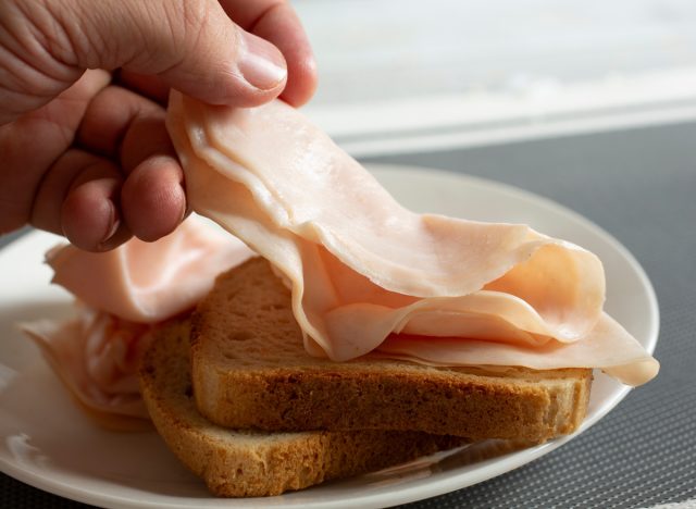 man laying down a slice of deli turkey on a slice of bread for a sandwich