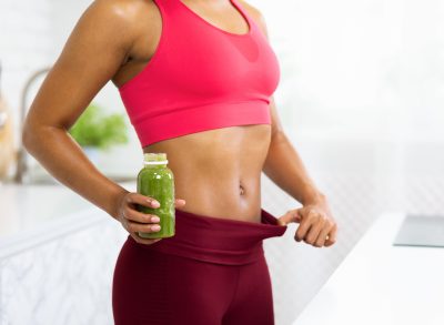 close-up woman holding workout leggings out with smoothie in the other hand, concept of how to lose belly fat without exercising