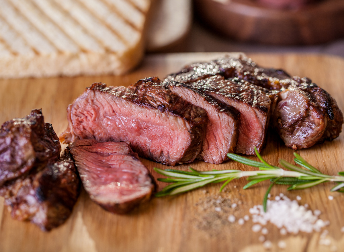 Grilled steak pieces with a sprig of rosemary, pepper and salt, fried pieces of bread on a wooden board. Horizontal orientation