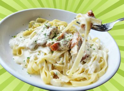 A bowl of fettucine Alfredo topped with chicken fritta at Olive Garden, set against a vibrant green background.