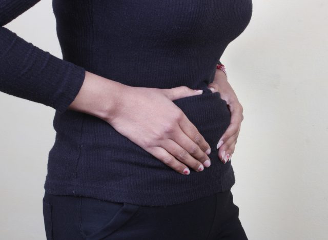 woman holding bloated belly, concept of belly fat or bloating