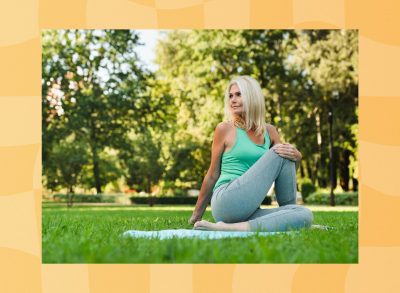 mature blonde woman stretching on blue yoga mat on grass, surrounded by trees and sunshine