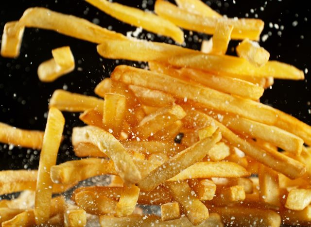 French fries - fried potatoes flying. Fly fastfood isolated on black background.