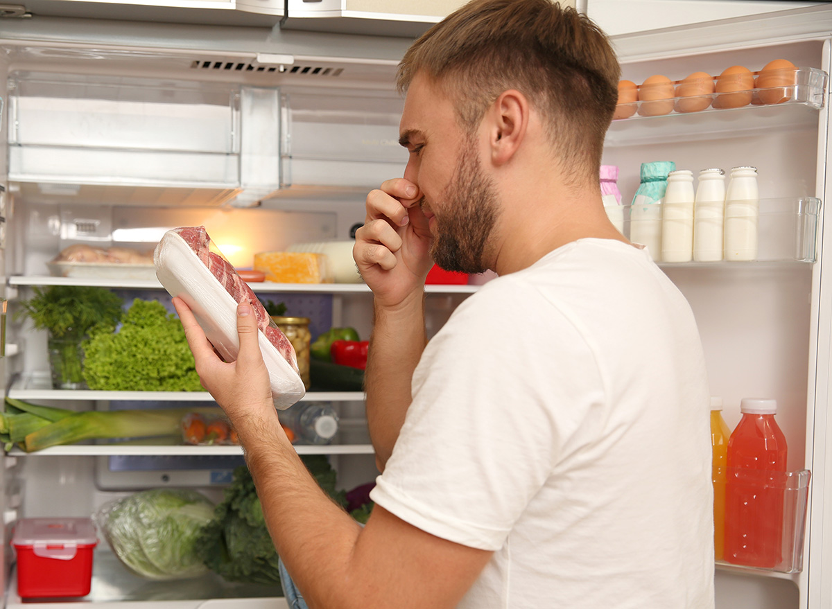 Young man with bad smelling meat near refrigerator in kitchen