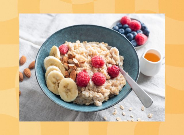 bowl of oatmeal with raspberries, slice banana, and almonds next to smaller bowl of berries and a little server of honey