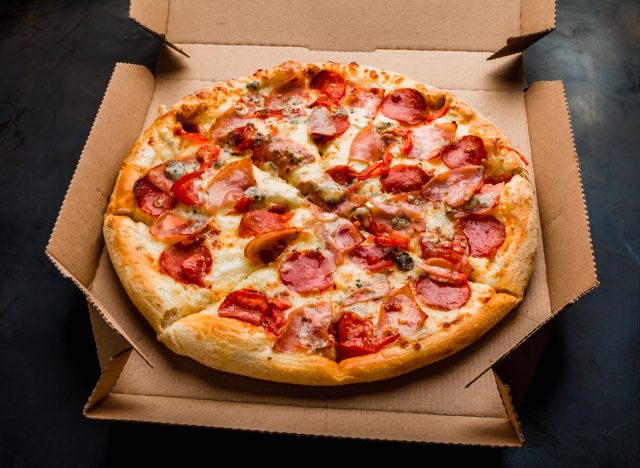 Pizza in a cardboard box against a dark background. Close-up. View from above. Pizza delivery. Pizza menu