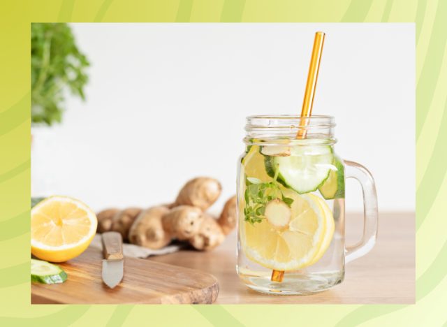 cucumber lemon ginger infused water in a glass next to a cutting board with a green border