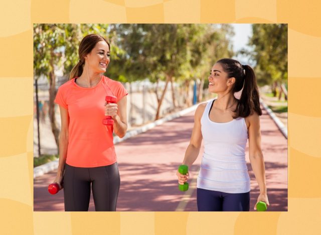 two happy women doing walking workout outdoors on track while holding dumbbells