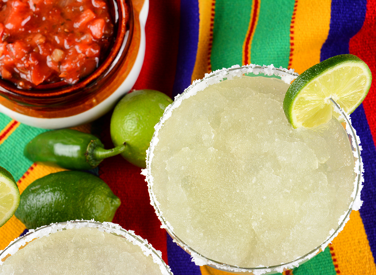 Margaritas and salsa on a colorful table cloth, with limes, and peppers.
