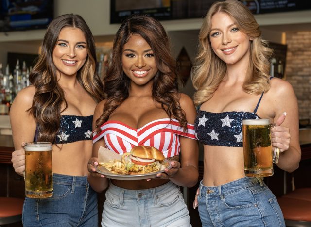 Three bikini-topped Hooters girls, carrying beers and a plate of burgers and fries