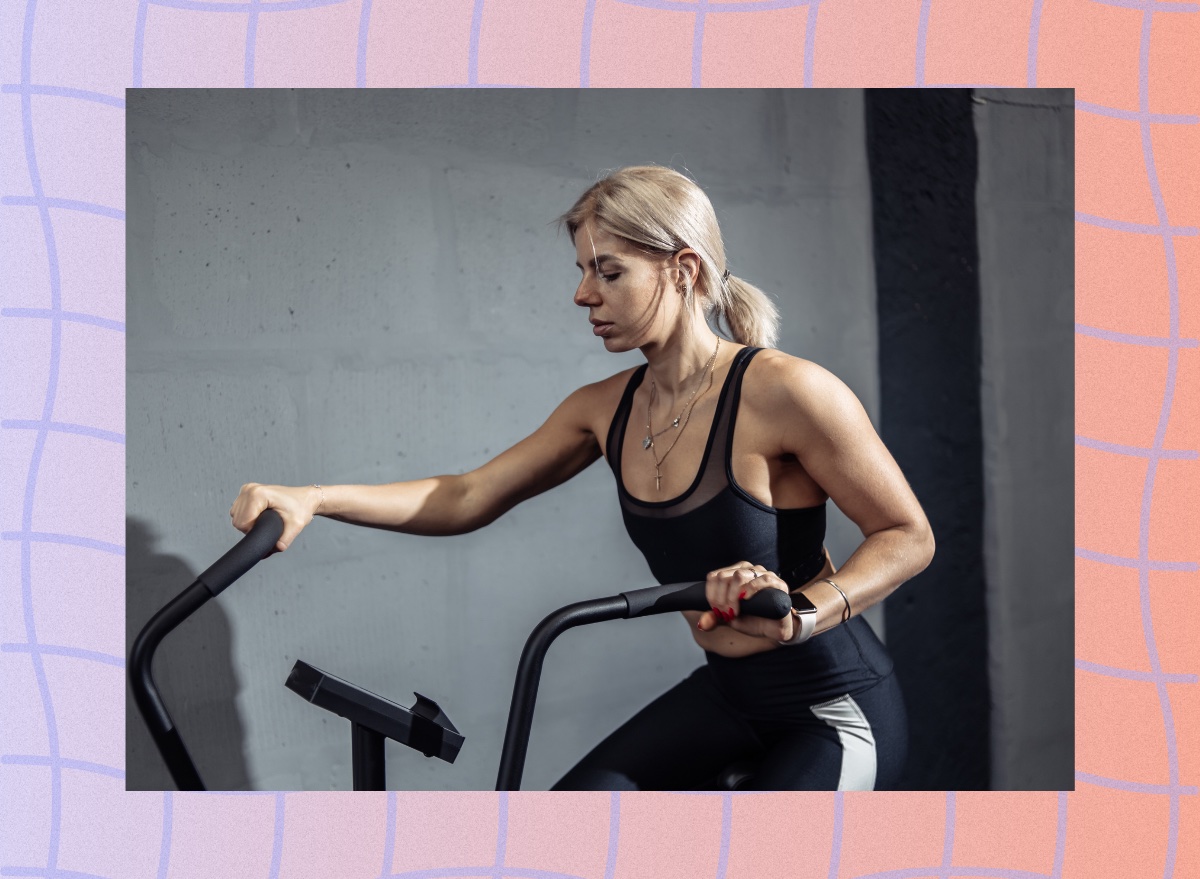 blonde woman at the gym using the air bike in front of gray cement wall