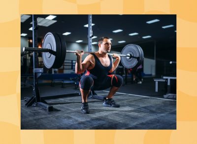 muscular man doing barbell back squat at the gym in darker room