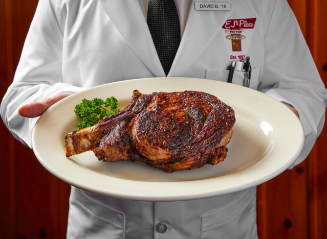 a man in a white coat holding a delicious looking plate of steak