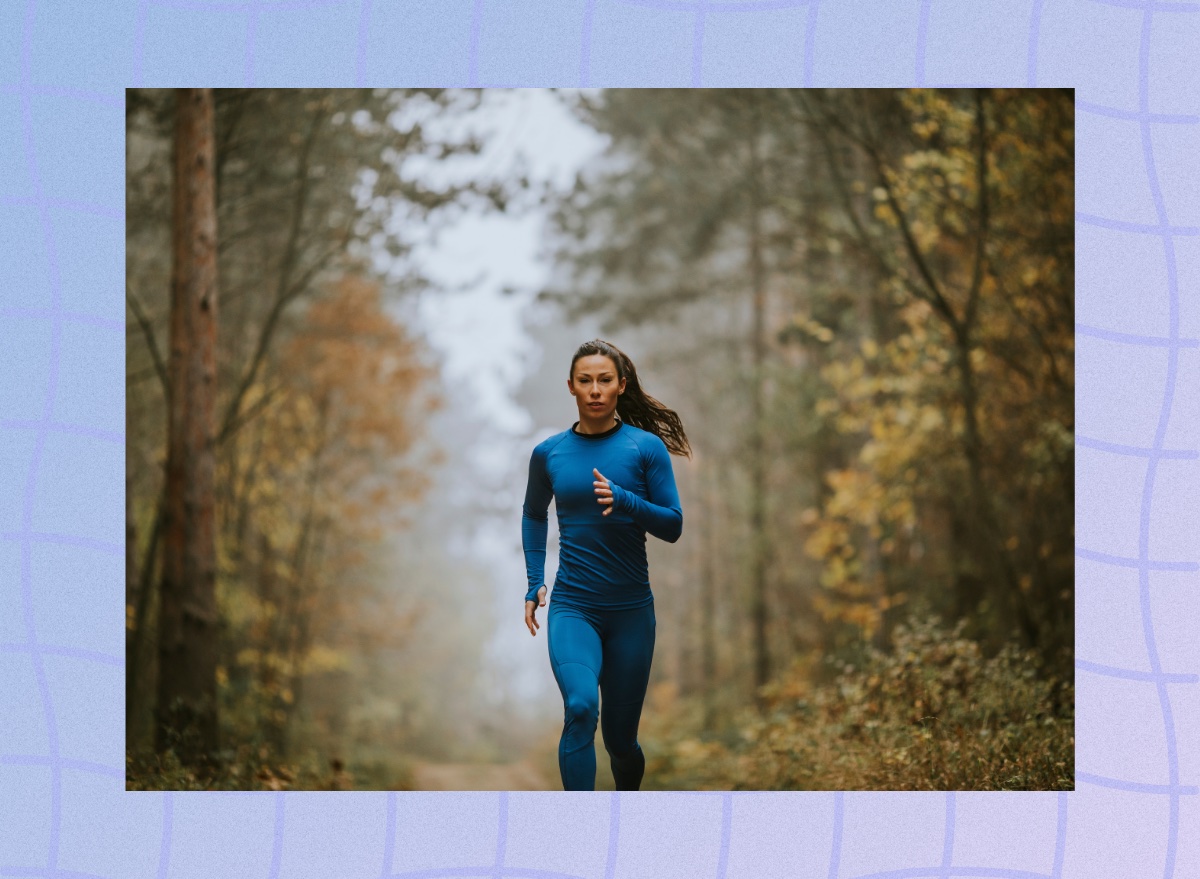fit, focused woman in blue athletic set running on trail surrounded by trees on hazy day