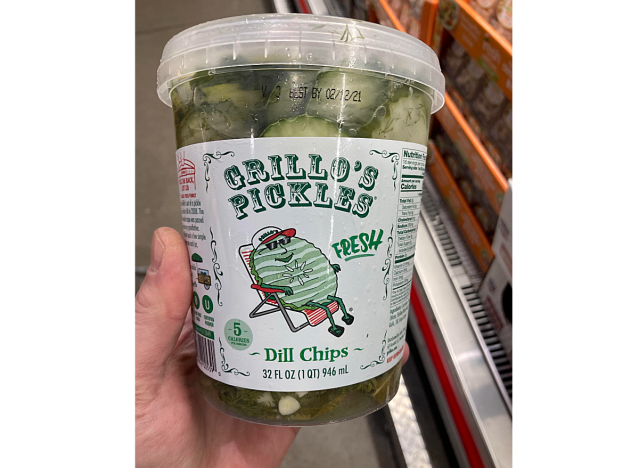 a hand holding a 32 ounce container of grillos pickle chips at costco