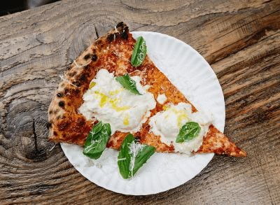 a slice of pizza with burratta and fresh basil on a wood table.