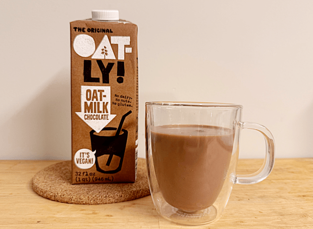a container of oatly chocolate oat milk next to a coffee mug
