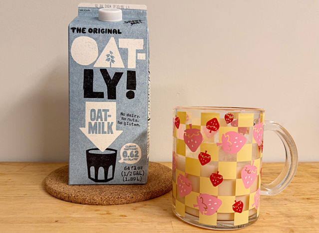 a container of oatly oat milk next to a strawberry printed mug