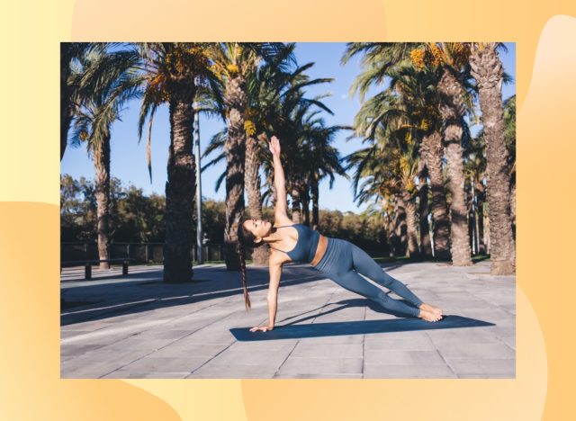 brunette woman with braid wearing blue fitness bra and leggings doing side plank on blue yoga mat surrounded by palm trees