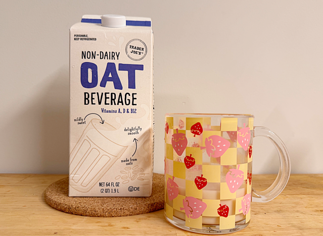 a container of trader joe's oat milk next to a mug with a strawberry print
