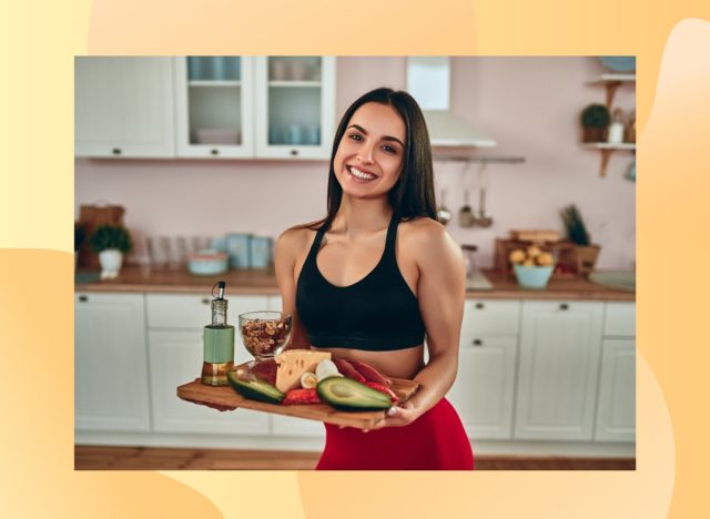 happy fitness woman holding tray of healthy, protein-packed foods in bright kitchen