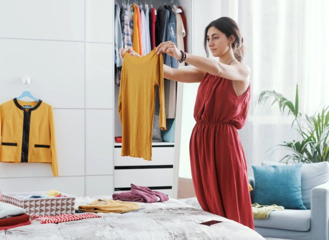 brunette woman organizing clothes in her bright bedroom