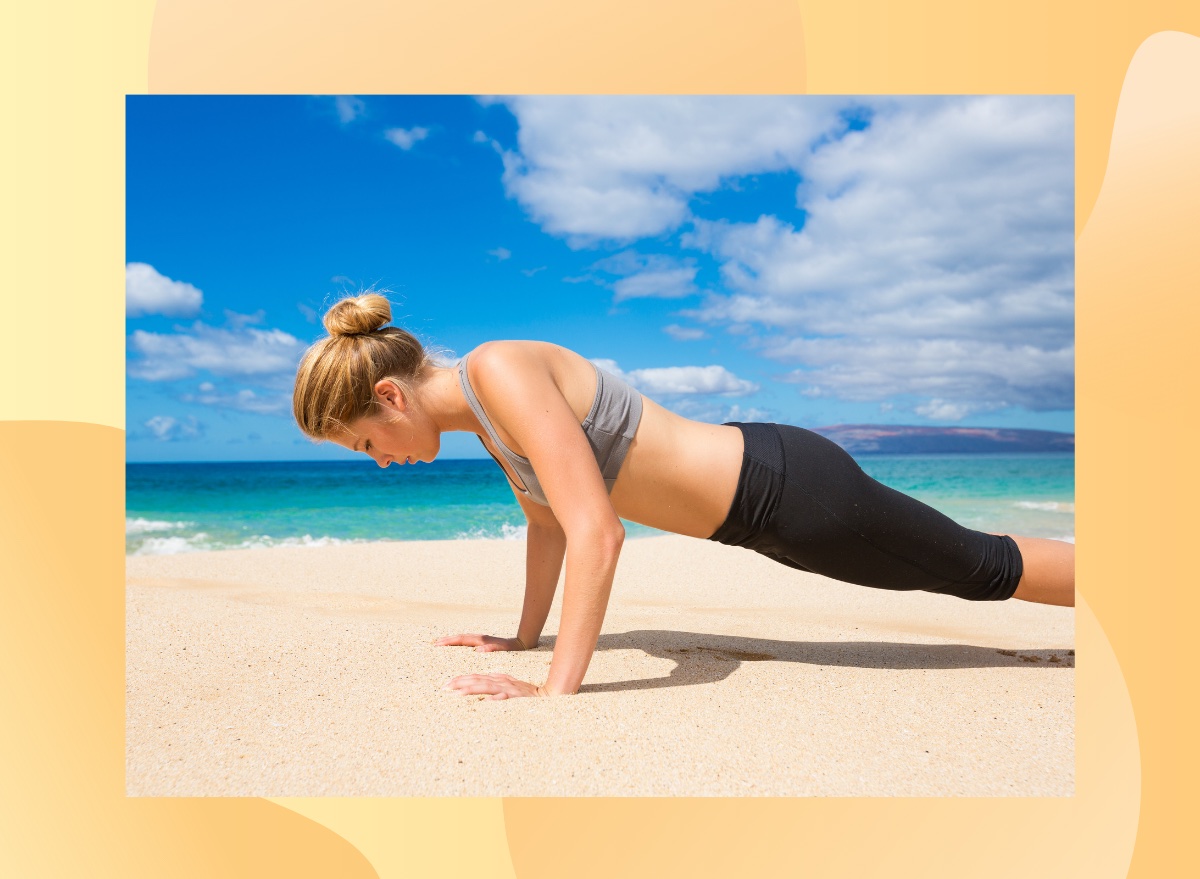 fit woman in sports bra and leggings doing pushups on sand at the beach by turquoise ocean water