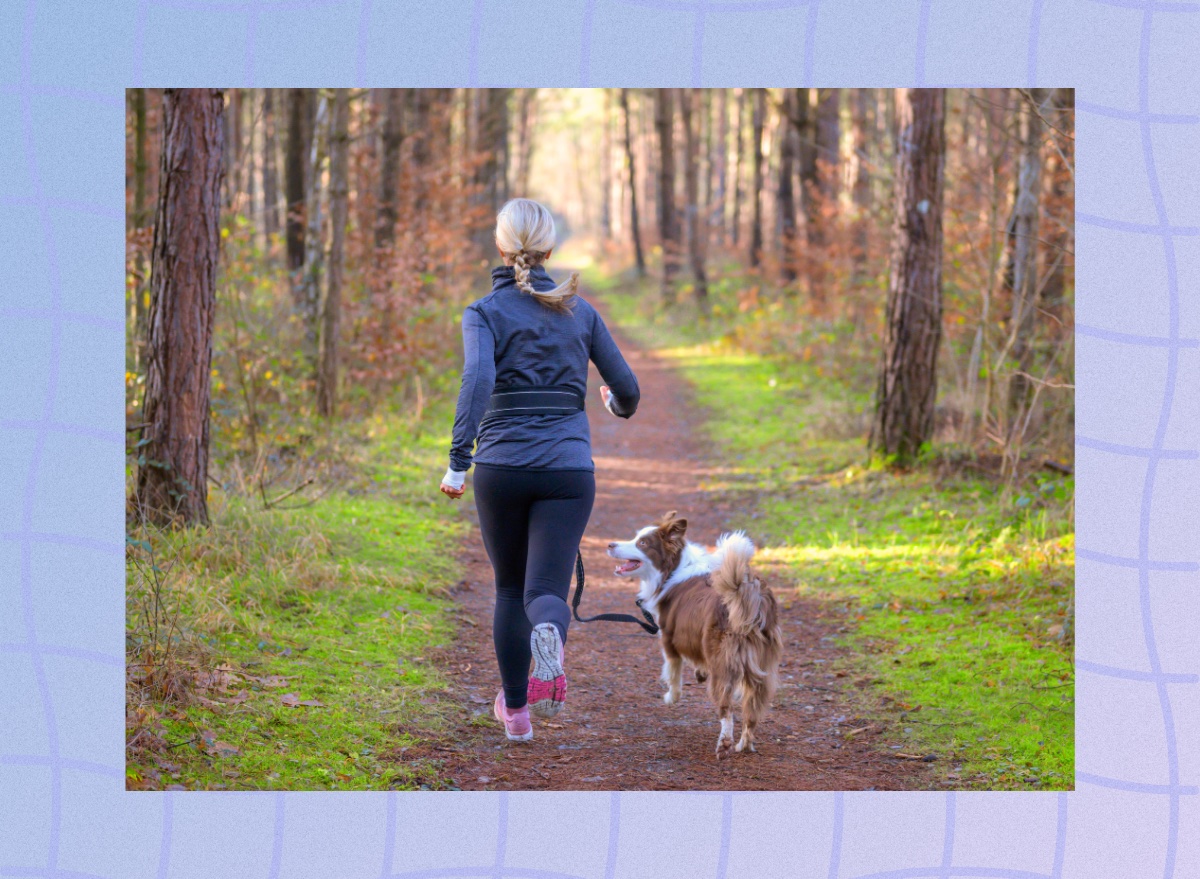 blonde woman running outdoors on trail surrounded by trees with her dog