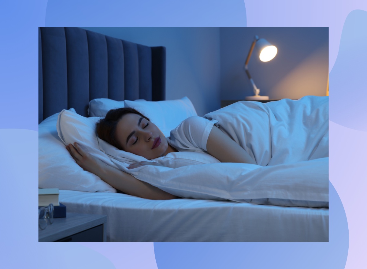 brunette woman sleeping peacefully in bed in dark room with small lamp on