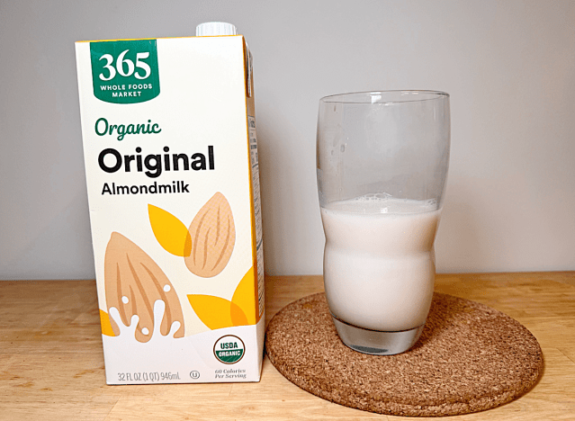 a container of 365 almond milk next to a glass of it 