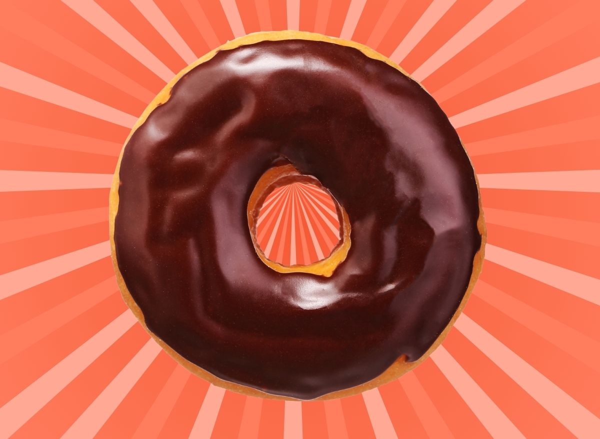 A chocolate-frosted doughnut set against a vibrant pink and red background