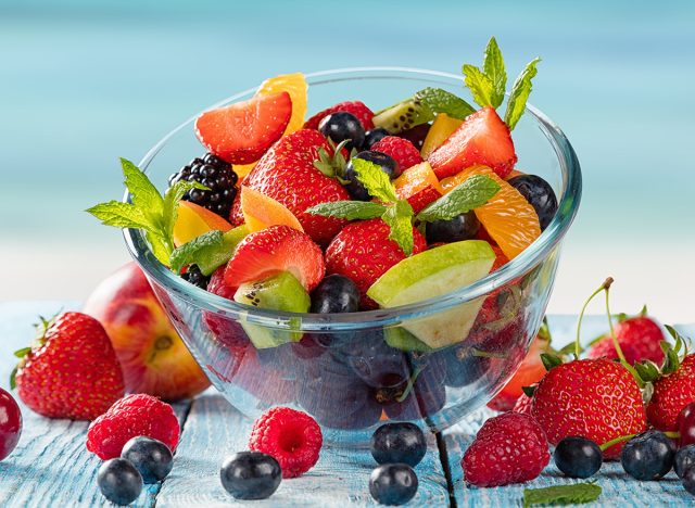 Fresh fruit salad placed on wooden planks with a blurry ocean in the background.