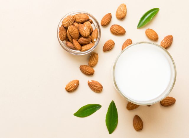 top level view of glass of almond milk with almonds scattered on flat lay