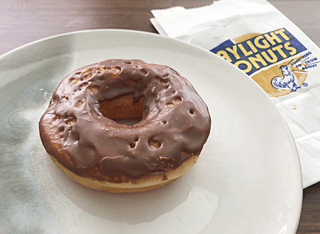 daylight donuts chocolate frosted on a plate next to a bag 