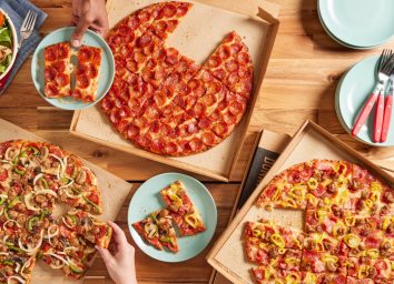 three donatos pizza pies on a wooden table with plates and hands taking slices of pizza