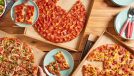 three donatos pizza pies on a wooden table with plates and hands taking slices of pizza
