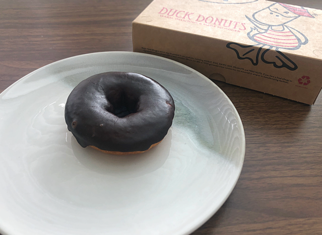 a chocolate glazed duck donut on a plate with a donut box 