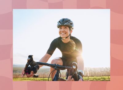 fit, happy woman riding bike outdoors for exercise by vineyard on sunny day